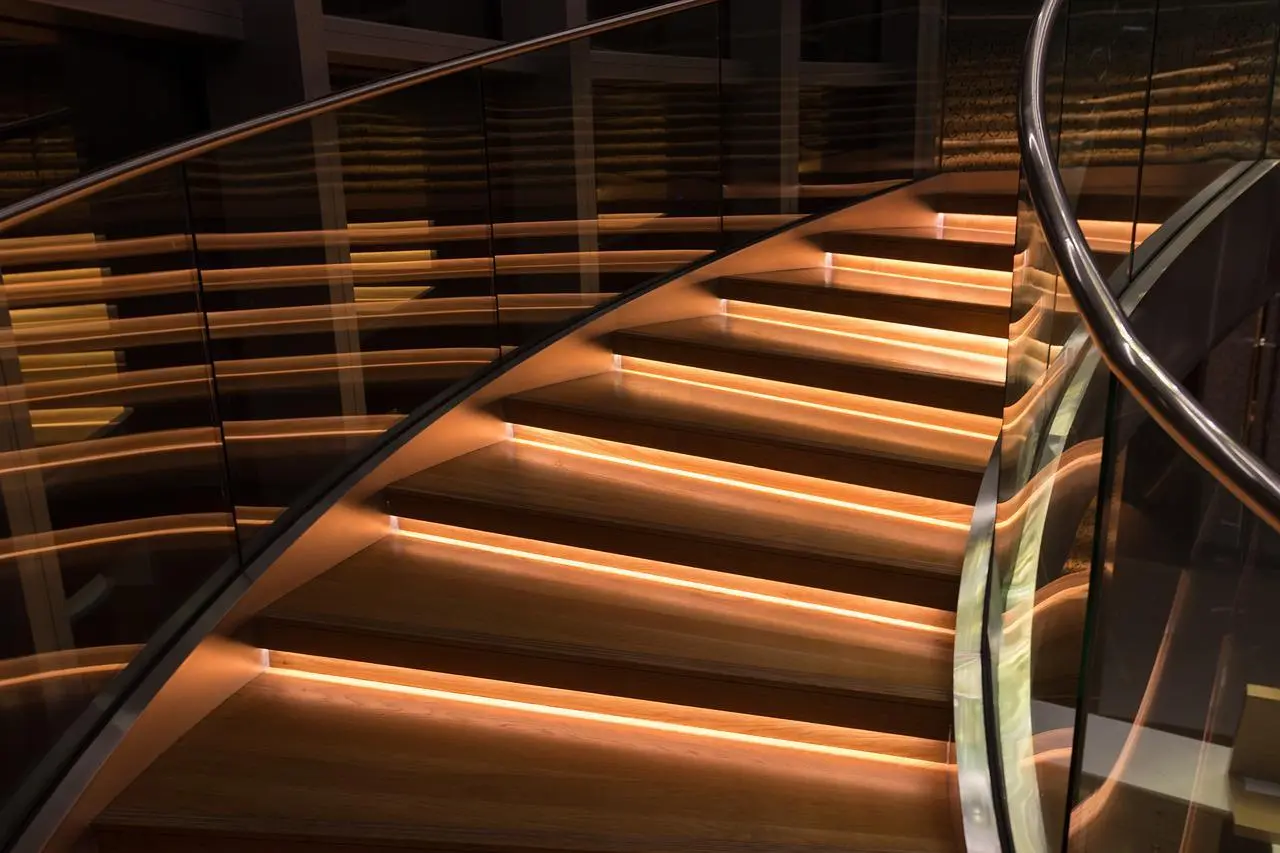 Modern staircase railing ideas: a curved staircase with a glass railing, a steel handrail and LED-lit wooden steps