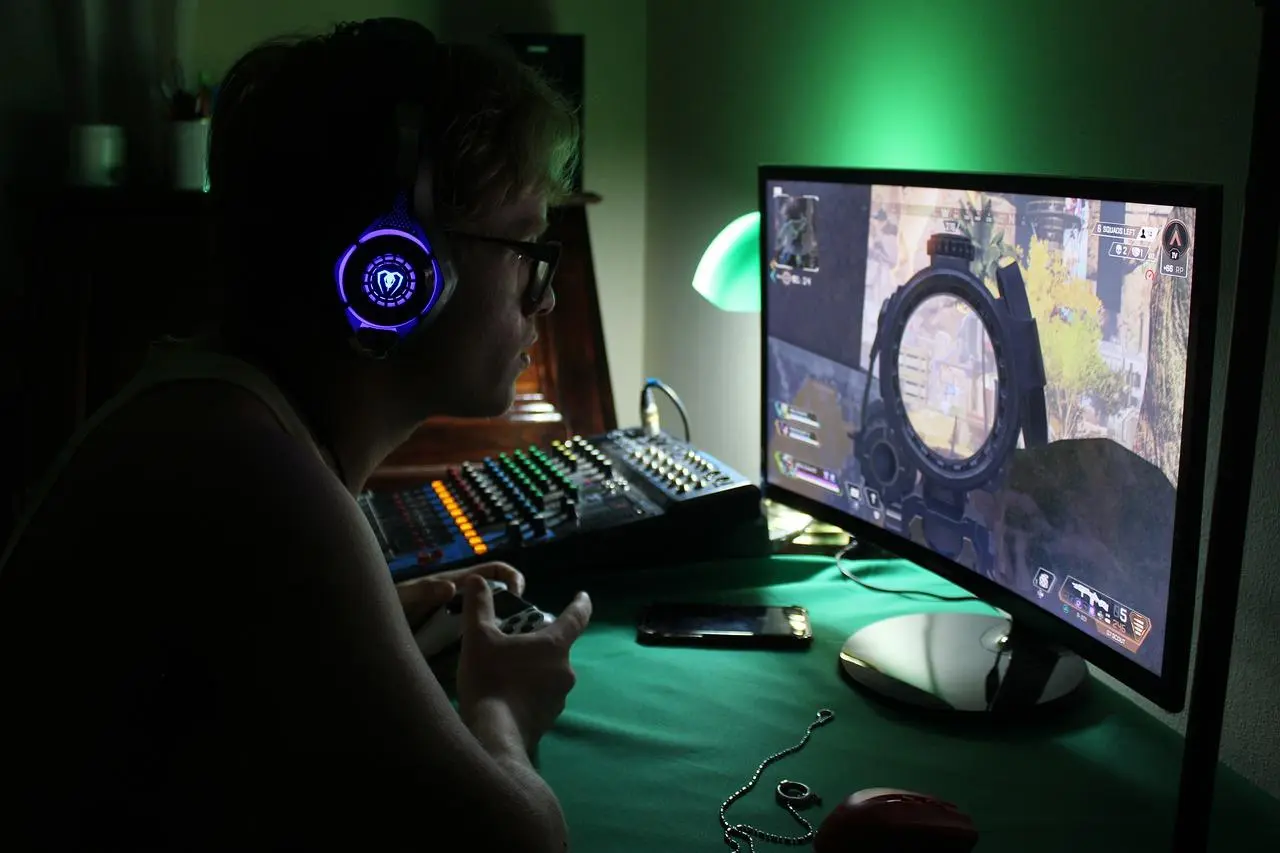Gamer with a lit headset at a desk with a monitor and mixer under green light