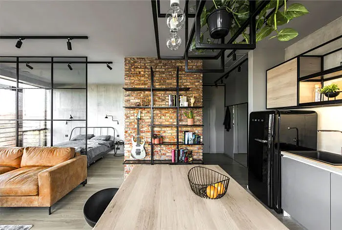 Industrial open-plan studio with a glass-walled bedroom, brick shelving and a leather sofa