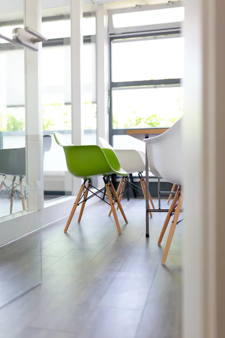 Glass-walled room with white and green moulded chairs on a grey wooden floor