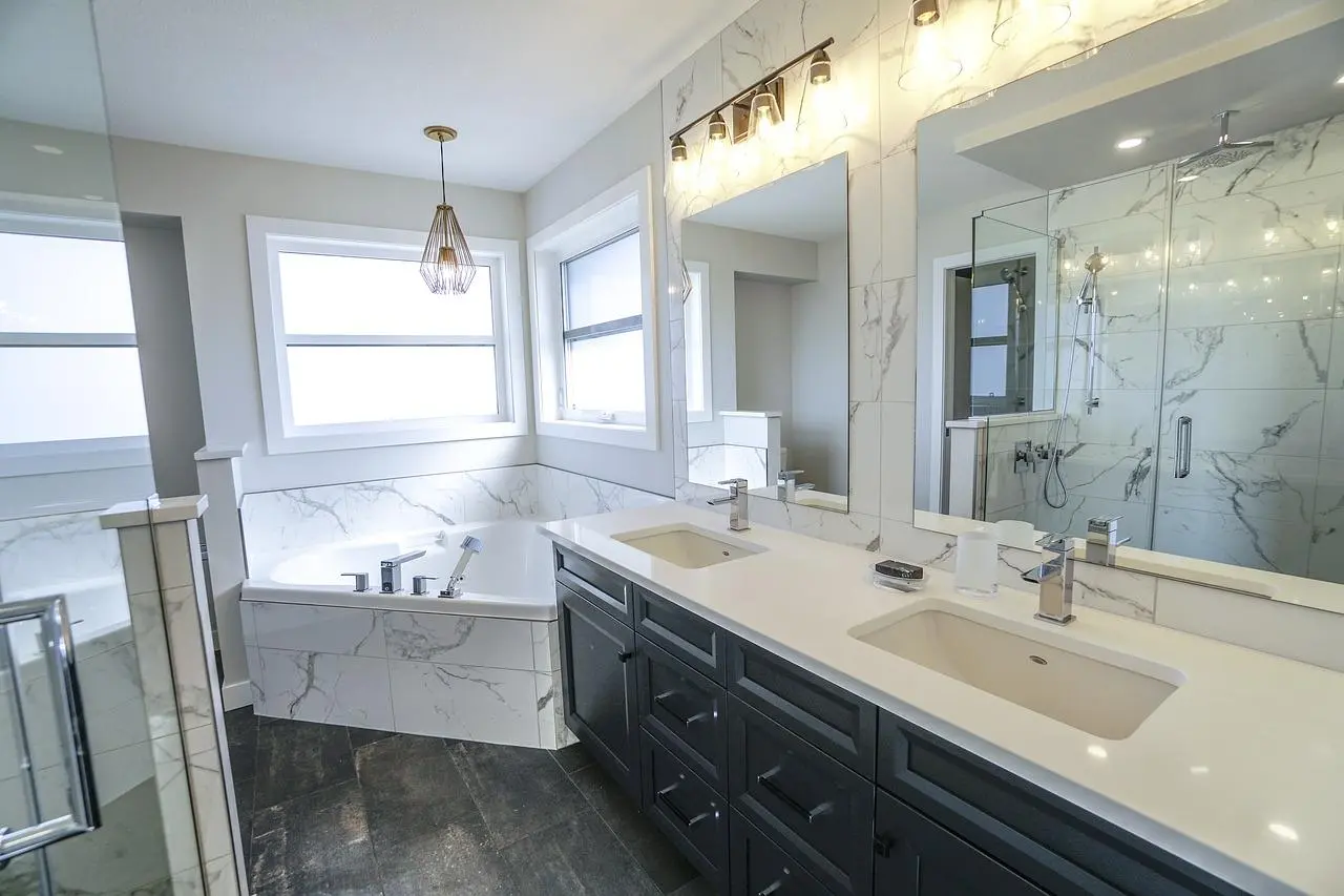 White marble bathroom with a double vanity, wall lights above the mirror and a corner tub