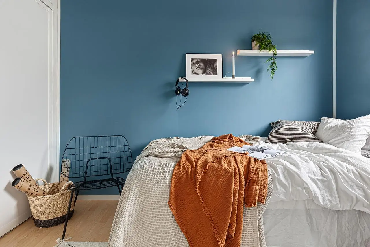 Calming bedroom colors: a soft blue wall with white bedding and an orange throw