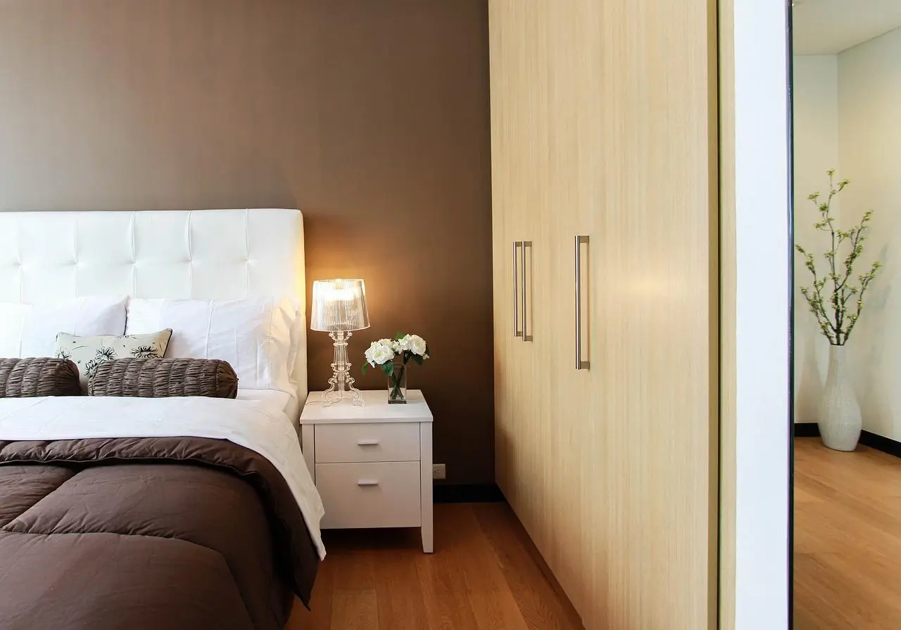 Bedroom with a chocolate brown wall, white headboard and light wood wardrobe