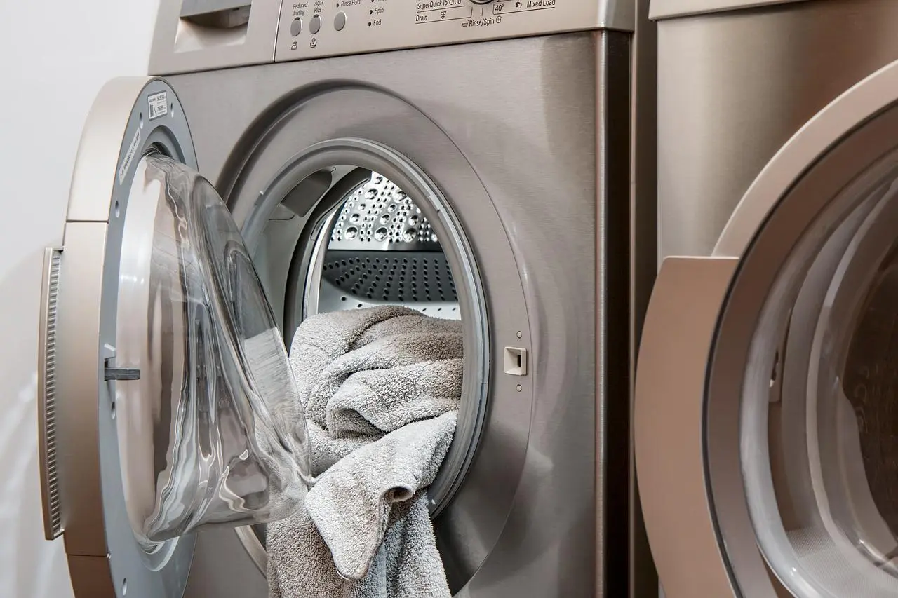 Front-loading washing machine with towels in an open drum next to a dryer