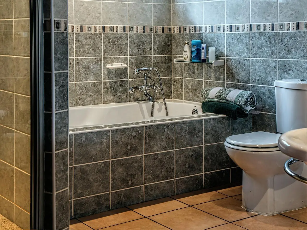 Bathroom with grey stone-look wall tiles, a bathtub and terracotta floor tiles