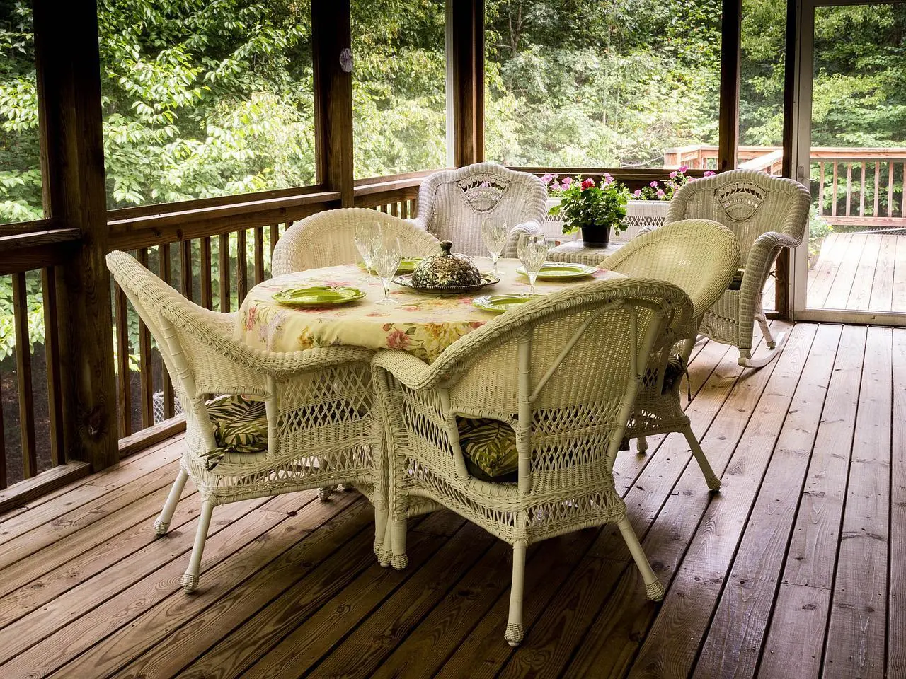 Deck de madera en pórtico techado con mesa para comer y sillas de mimbre blanco